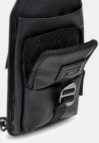 Borsa a tracolla nera in nylon con tasca con cerniera, superficie testurizzata, etichetta con logo e dettagli in metallo argentato.