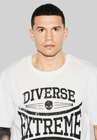 Biała bawełniana koszulka z czarnym nadrukiem graficznym z napisem "DIVERSE EXTREME" i czaszką. Krótkie rękawy, okrągły dekolt, standardowy krój.
