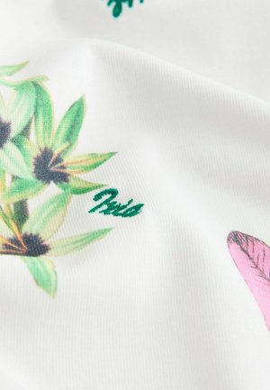 Tissu avec un motif floral vert et noir et une petite forme rose sur fond blanc, montrant la texture et les plis.