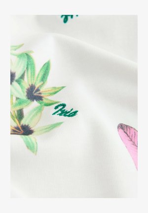 Tissu avec un motif floral vert et noir et une petite forme rose sur fond blanc, montrant la texture et les plis.