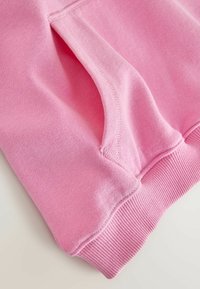 Sweat-shirt rose avec une texture lisse, doté d'une poche latérale et de poignets côtelés. Le tissu présente un motif tricoté fin.