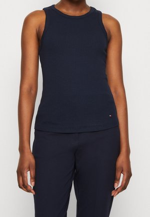 Person wearing a sleeveless, navy ribbed tank top and matching navy pants, standing against a plain light background.