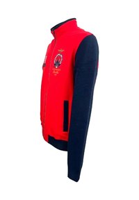 Giacca in pile rossa e blu navy con maniche lunghe, chiusura frontale con zip, tasche laterali e logo ricamato sul petto. Accenti in cuciture dorate.