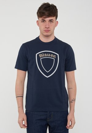 Marineblå t-shirt lavet af bomuld med korte ærmer, der har et stort, lyst skjoldlogo med teksten "Blauer." Trykt design foran.