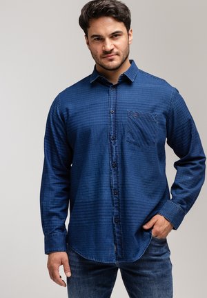 Granatowa, w kratkę, koszula z długim rękawem z zapięciem na guziki i kieszonką na piersi, wykonana z teksturowanego materiału, zestawiona z niebieskimi dżinsami.