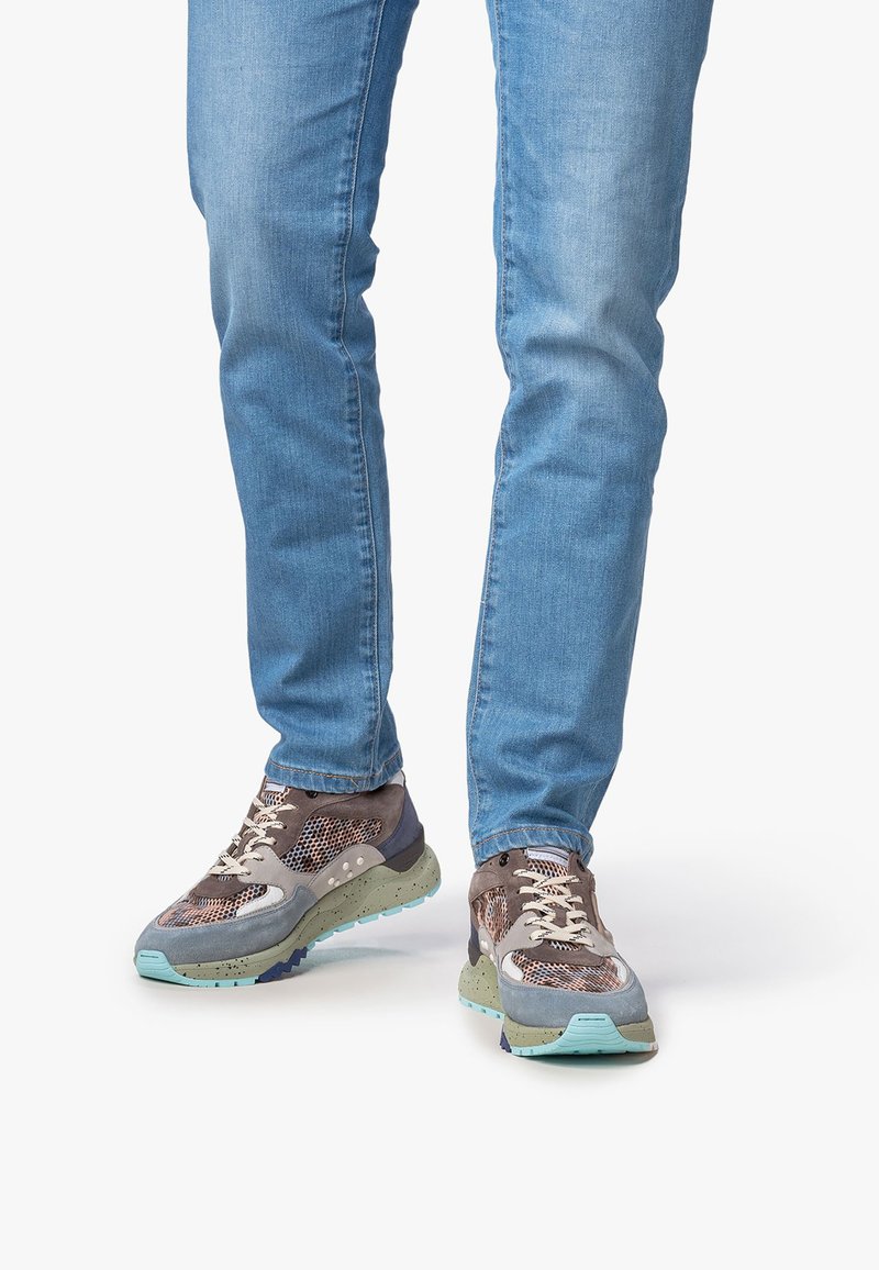 Sneakers con una toma in mesh, marrone e grigia, lacci a contrasto e una suola chunky, maculata in tonalità blu chiaro e verdastre.