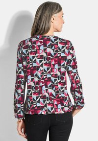 Langsleeve blouse in een geometrisch patroon met rode, blauwe, zwarte en witte vormen; gemaakt van een soepele, lichte stof met een gerimpelde zoom.