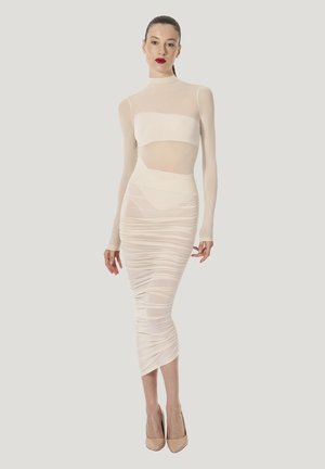 Figurnära, genomskinlig långärmad topp kombinerad med en rynkad, knälång kjol i offwhite. Slingbacks i nudefärg fulländar looken.