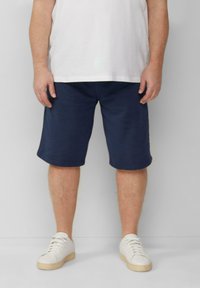 Marineblauwe katoenen shorts met een elastische tailleband. Draagt een wit T-shirt en witte sneakers met een beige zool.