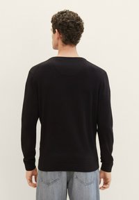 Pulover negru cu mâneci lungi, textura cu nervuri, guler rotund și manșete strânse. Purtați cu blugi de culoare albastră deschisă, evidențiind un croi lejer.