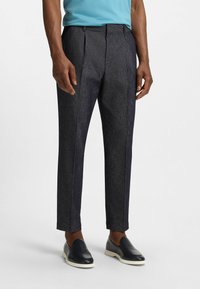 Dark gray tailored trousers with a textured finish, pleats at the front, and contrasting side stripes, paired with black loafers.