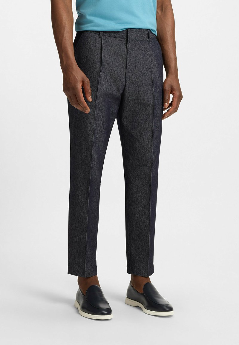 Donkergrijze op maat gemaakte broek met een gestructureerde afwerking, plooien aan de voorkant en contrasterende zijkanten, gecombineerd met zwarte instappers.