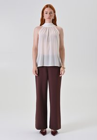 Top bianco senza maniche in tessuto leggero, abbinato a pantaloni larghi color borgogna scuro e tacchi a punta color borgogna. Silhouette semplice e morbida caduta.
