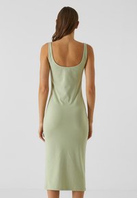 Robe midi élégante et ajustée en tissu vert clair. Elle présente un dos en forme de cœur, des bretelles fines et une texture lisse avec des coutures minimales.