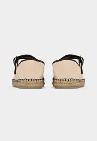 Paire de sandales espadrilles beige avec garniture noire et brides à la cheville, vue de dos sur un fond uni.