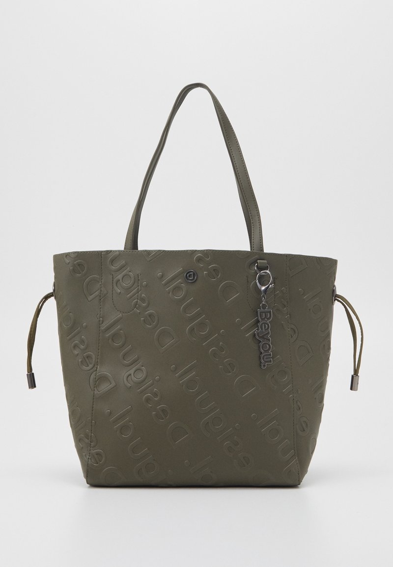 Sac fourre-tout vert olive avec logo embossé, deux longues poignées, cordons latéraux réglables et un pendentif argenté en guise d'accent.