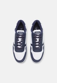 Sneaker navy e bianco con superiore in tessuto e suede, punta rotonda, design con lacci, suola in gomma e marchio Lacoste sulla linguetta.