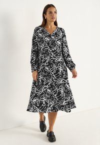 Schwarzes Kleid mit weißem Blumenmuster, langen Ärmeln, V-Ausschnitt und kniefrohem Rock. Aus glattem Stoff gefertigt, mit einem klassischen, fließenden Design.