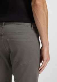 Szare, dopasowane spodnie wykonane z gładkiego materiału. Charakteryzują się minimalistycznym designem, subtelnym przeszyciem oraz metką z logo na pasku.