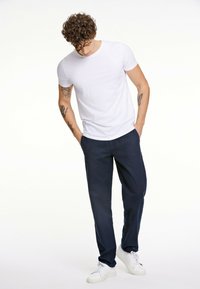Camiseta blanca de manga corta combinada con pantalones tapered en color marino y zapatillas blancas. La tela parece suave, con un diseño ajustado y un aspecto casual.