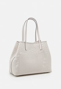 Sac fourre-tout blanc avec des perforations en forme de losange, une bordure noire et deux longues poignées, posé sur une surface blanche.