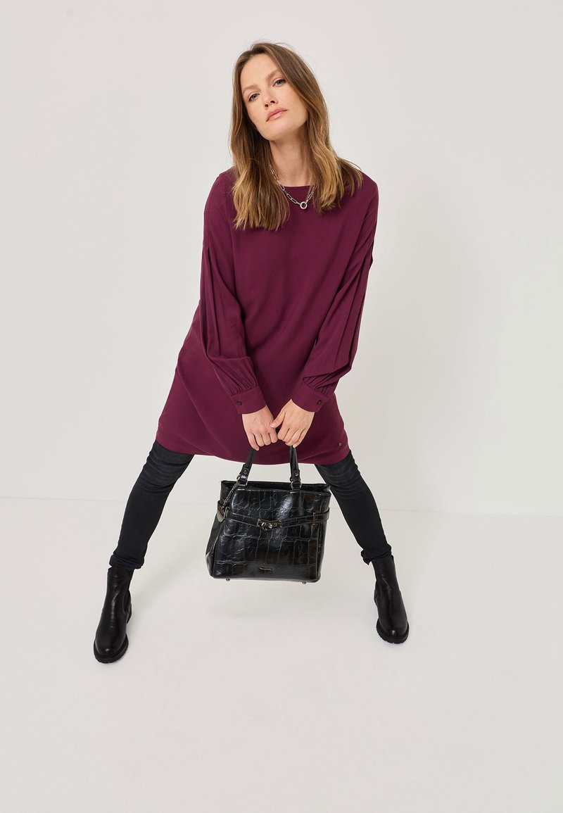 Burgundia pitkähihaine mekko, jossa on kootut hihat, yhdistetty mustiin slim-fit-farkkuihin ja nilkkureihin. Musta krokopintainen käsilaukku, metalliset yksityiskohdat.