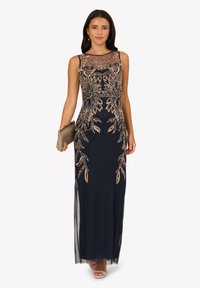 Navy-blaues langes Kleid mit aufwendiger goldener Stickerei, transparenter Ausschnitt und taillierter Silhouette. Ergänzt durch eine goldene Clutch und offene High Heels.
