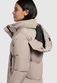 Gai bēša krūšu jaka ar augstu apkakli, ar rāvējslēdzēju priekšpusē, sānu kabatām un noņemamu kapuci, ar gludu, teksturētu apdari.