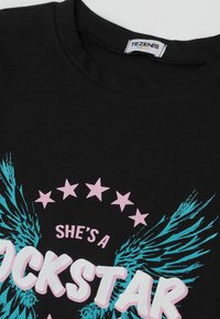 Schwarzes Baumwoll-T-Shirt mit blauen Flügelgrafiken und rosa Text, der "SHE'S A ROCKSTAR" liest, mit rosa Sternakzenten über dem Text.