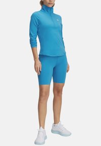 Lichtblauw sporttop met hoge kraag, lange mouwen en een ritssluiting, gecombineerd met bijpassende hoge shorts en witte sneakers.