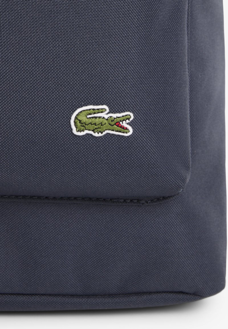 Tessuto blu scuro strutturato con un piccolo logo di coccodrillo verde ricamato con bocca rossa aperta sulla tasca frontale.