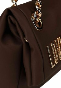 Dettaglio ravvicinato di una borsa in pelle marrone scuro con tracolla in catena dorata e la scritta "LOVE" dorata sul davanti.