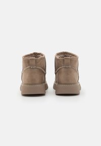 Botas de tobillo de ante en color tostado con un forro suave, que presentan una pestaña en la parte trasera, costuras decorativas y una suela de goma resistente.