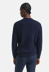 Marineblauer Strickpullover mit Zopfmuster, gerippten Bündchen und Saum. Die Rückansicht zeigt einen lässigen Schnitt und strukturierte Stoff.