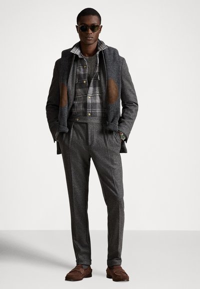 Szara marynarka z mieszanki wełny z brązowymi łokciami, noszona na koszuli w kratę. Szare dopasowane spodnie i brązowe mokasyny dopełniają strój.