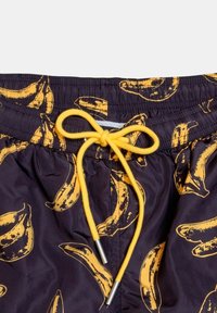 Pantaloni da bagno neri con una stampa di banane gialla ripetuta, con vita elastica e un cordino giallo con estremità metalliche.