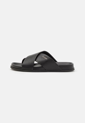 Black slide sandal with crossed straps and flat sole. Made of synthetic material, featuring a sleek design and a gold logo accent.
