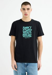 Camiseta de algodón negra con texto en verde menta que dice "NO TE PREOCUPES POR EL FUTURO" en una tipografía divertida. Ajuste casual y diseño de cuello redondo.