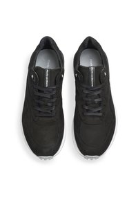 Zapatillas deportivas negras con parte superior de tela texturizada, diseño con cordones y cuello acolchado. Presentan una suela blanca y acentos de logo reflectantes.