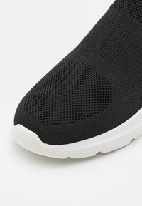 Scarpa sportiva nera con tomaia in maglia e superficie texturizzata, dotata di suola in gomma bianca e design senza cuciture.