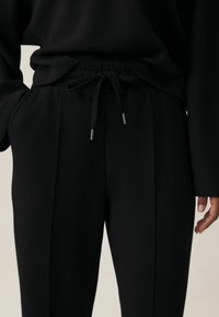 Zwarte broeken gemaakt van zachte stof, met een elastische tailleband met trekkoorden en elegante voorplooien. Geschikt voor casual wear.