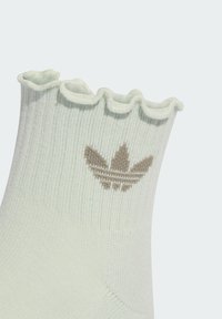 Svijetlozeleni čarapa s naboranim gornjim rubom i utkanim smeškim Adidas logotipom. Izrađena od mekog, teksturiranog pamuka.