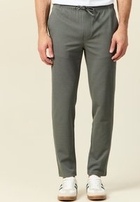 Grijze sweatpants met een elastische tailleband en trekkoord, met een tapere pasvorm en een gladde textuur. Gemaakt in combinatie met witte sneakers.