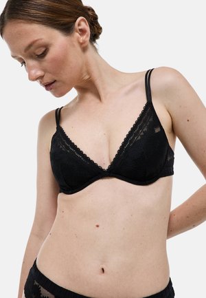 Soutien-gorge en dentelle noire avec des bonnets triangulaires, présentant de délicates bordures festonnées et des bretelles ajustables fines. Texture douce, design minimaliste.