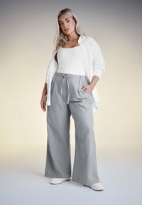 Grå randiga vida byxor med knyt i midjan, kombinerat med en vit linne och en öppen vit skjorta. Slät tygtextur.