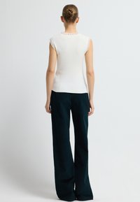 Hvid ribbet ærmeløs top med en flæset halsudskæring, parret med mørke, brede bukser. Glat tekstur og tætsiddende form med sideslids.