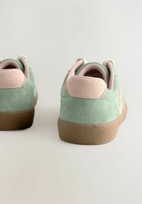 Grüne Wildleder-Sneaker mit einer hellrosa Fersenlasche und Akzenten. Gummilaufsohle mit strukturiertem Muster. Gepolsterter Kragen für Komfort.