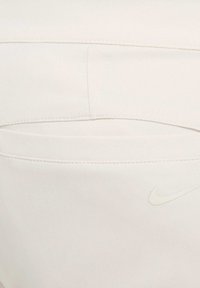 Baltas bikses, kas izgatavotas no teksturēta auduma ar zigzagveida rakstu. Tām ir aizmugures kabata un diskreta Nike logo, kas ir saskaņotā krāsā.