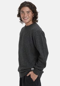 Dunkelgrauer, gesprenkelter Pullover mit Rundhalsausschnitt und gerippten Bündchen. Verfügt über ein Logo-Label am Saum. Material wirkt gestrickt und strukturiert.