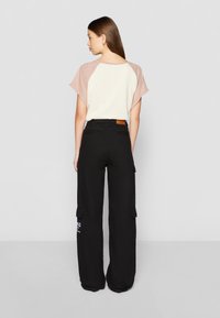 Short-sleeve top with beige body and light pink sleeves, paired with black cargo pants featuring side pockets and white text detail.